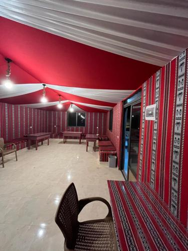 a room with red walls with benches and tables at Sandy Camp Wadi Rum in Wadi Rum