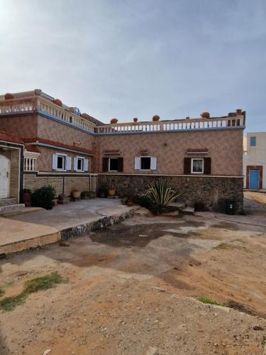 Un gran edificio de ladrillo con un patio delante. en Maison bord de mer, en Zaouia Sidi Ouaggag