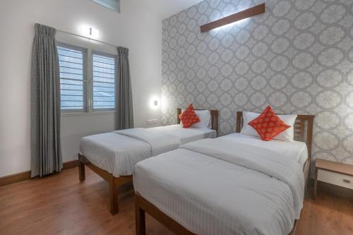 a bedroom with two beds with white sheets and red pillows at Ixora Suites in Bengaluru
