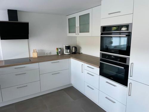 a white kitchen with white cabinets and black appliances at Ferienapartment Auszeit- Sauna, Whirlpool und Garten zur Alleinnutzung in Traben-Trarbach