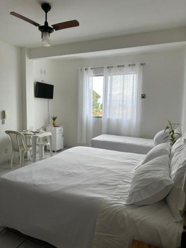 a white bedroom with a large bed and a table at Residencial Castelinho in Mucuri