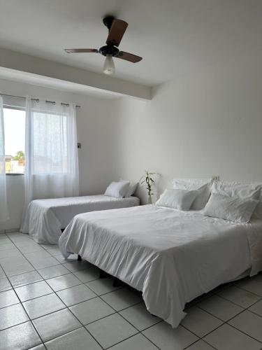 a white bedroom with two beds and a ceiling fan at Residencial Castelinho in Mucuri