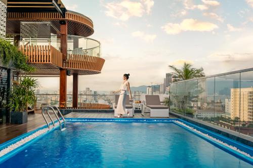 a woman standing next to a swimming pool on top of a building at Mercy Emerald Hotel in Danang