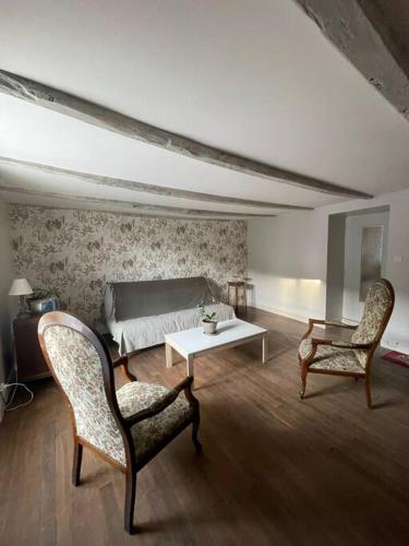a living room with two chairs and a table and a bed at La maison du sabotier in Oradour-Saint-Genest