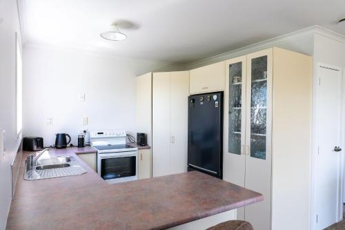 a kitchen with white cabinets and a black refrigerator at Fantail Cottage in Hamilton