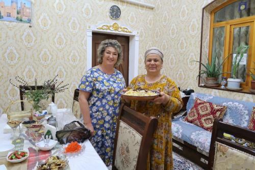 dos mujeres de pie en una habitación sosteniendo un plato de comida en Khiva Ibrohim Guest House, en Khiva