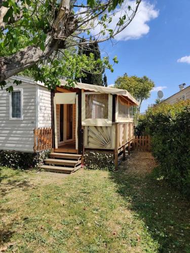 a tiny house with a porch next to a yard at MOBIL HOME CLIMATISE 2 CHAMBRES CLIMATISE CAMPING 4 ETOILES LE LAC DES REVES in Lattes