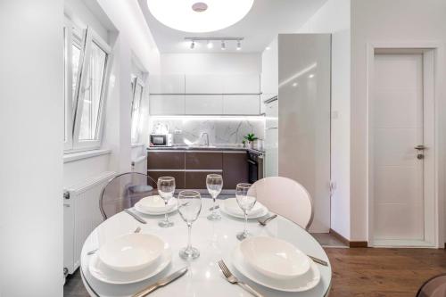 - une table à manger blanche avec des assiettes et des verres à vin dans l'établissement Silver Apartment, à Novi Sad