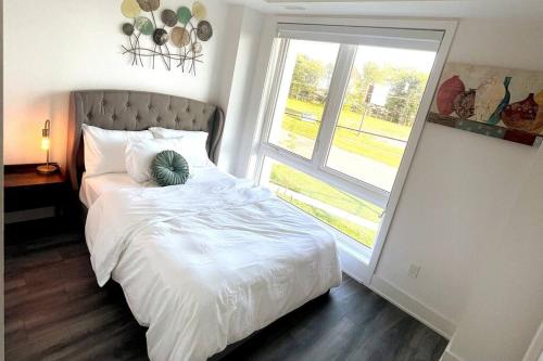 a bedroom with a white bed with a large window at Exquisite, bright & modern condo. in Niagara Falls