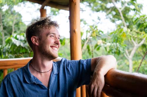 a man in a blue shirt sitting on a porch at Dave the Cave Eco Lodge and Cultural Campsite in Rubirizi
