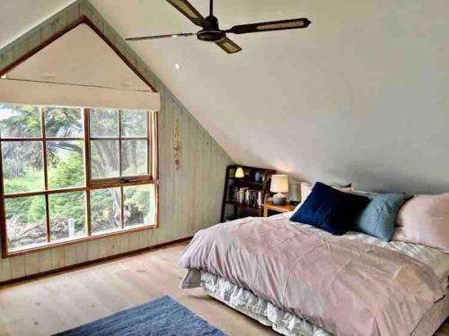 a bedroom with a bed with a ceiling fan and a window at Alyeska Loft - Apollo Bay studio loft apartment in Apollo Bay