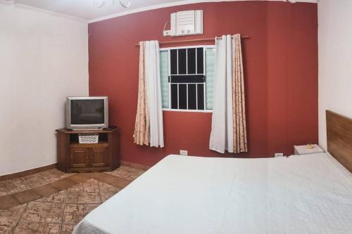 a bedroom with a bed and a tv and a window at CASA JD SÃO LOURENÇO PISCINA AR WI-FI TV PRAIA in Bertioga