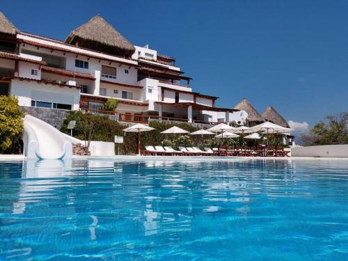 a swimming pool in front of a hotel with umbrellas at IXTAPA Zihuatanejo Alegria y Familia in Ixtapa