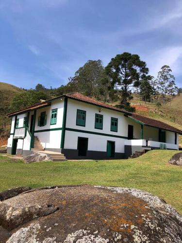 ein weißes Haus mit grünem Trimm auf einem Feld in der Unterkunft Fazenda Vô Azarias in Visconde De Maua