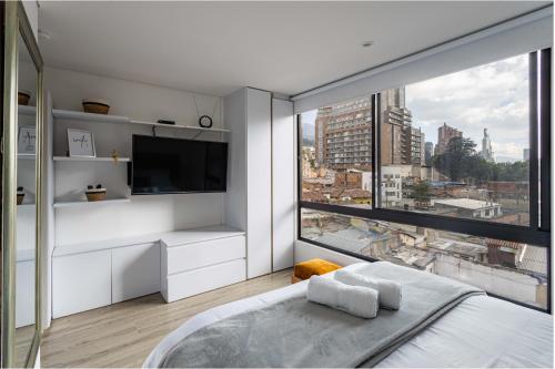 a white bedroom with a large window and a tv at Loft nuevo, moderno, central in Bogotá