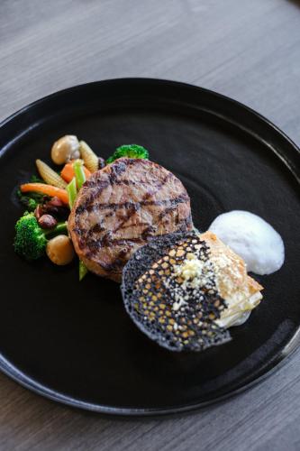 a black plate with a steak and vegetables on it at Amartahills Hotel and Resort in Batu