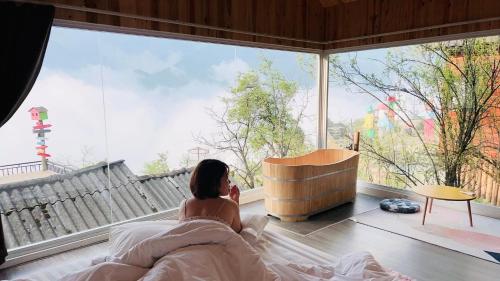 a woman sitting in bed looking out of a large window at Daisy Sapa - Homestay - Panorama in Lao Cai