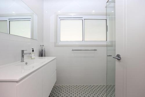 a white bathroom with a shower and a sink at Wylah in North Arms Cove