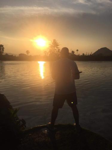a man standing in front of a lake at sunset at Ban Por Fai in Cha Am