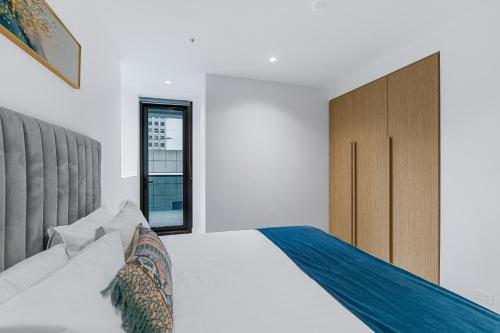 a white bedroom with a large bed and a window at Collins House Apartments by CLLIX in Melbourne