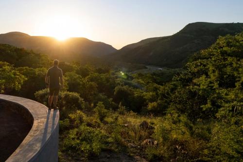 a man standing on a ledge looking at the sunset at Matatane Camp - Babanango Game Reserve in Nkwalini