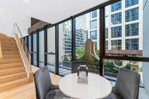 a table and chairs in a room with a large window at Collins House Apartments by CLLIX in Melbourne