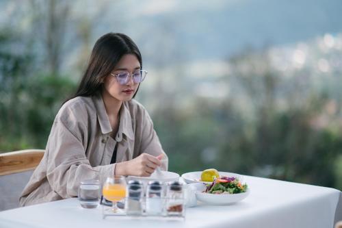 a woman sitting at a table with a plate of food at Arabica Lodge (อาราบิก้า ลอดจ์) in Ban Huai Khai