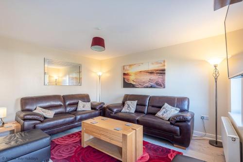 a living room with a leather couch and a table at Greenwich Cottage - Part of the The Bay Filey Holiday Village with pool, gym and direct beach access, pub, restaurant, tennis and meadows walks in Reighton