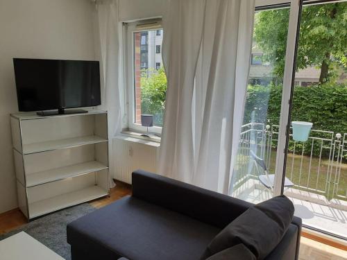 ein Wohnzimmer mit einem Sofa, einem TV und einem Fenster in der Unterkunft Perfektes Appartement am Düsseldorfer Rhein in Düsseldorf