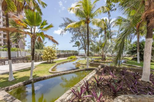 un jardín con palmeras y un estanque en Flat Edf Golden Beach, en Jaboatao dos Guararapes