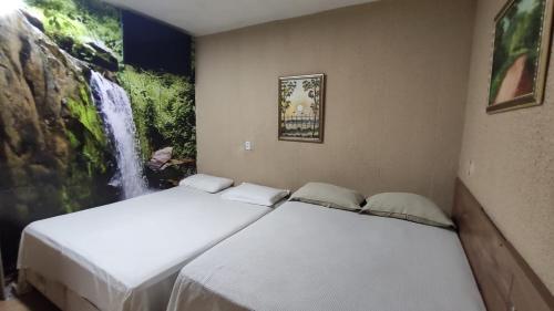 two beds in a room with a waterfall painting on the wall at Hotel Nacional in Sobral