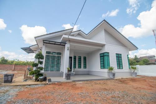 Casa blanca con ventanas con persianas verdes en Romi Homestay Wakaf Tapai en Marang