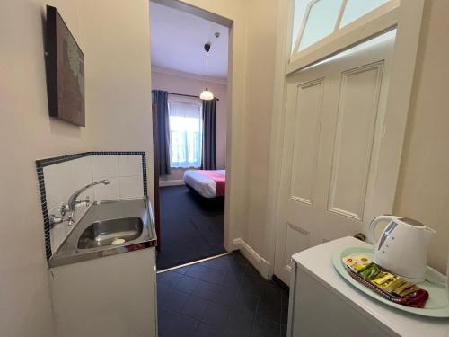 ein kleines Bad mit einem Waschbecken und ein Zimmer mit einem Bett in der Unterkunft Princes Lodge Motel in Adelaide