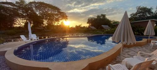 a swimming pool with chairs and umbrellas and the sunset at Bua Daeng Homestay Resort in Amphoe Kumphawapi