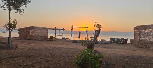 een strand met twee hutten en de oceaan bij zonsondergang bij Michael's House in Nuweiba