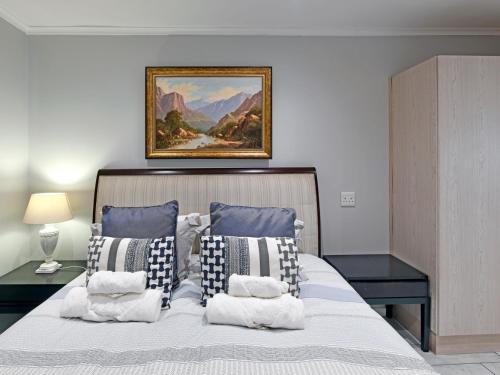 een slaapkamer met een bed met kussens en een schilderij aan de muur bij La Rochelle Cottage in Franschhoek