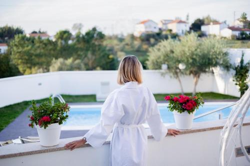 a woman in a white dress standing on a balcony with flowers at Jasmine Hotel in São Pedro de Alva