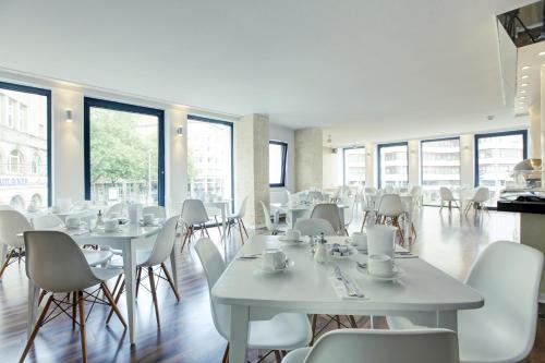 un restaurante con mesas y sillas blancas y ventanas en Smartcity Designhotel, en Hannover