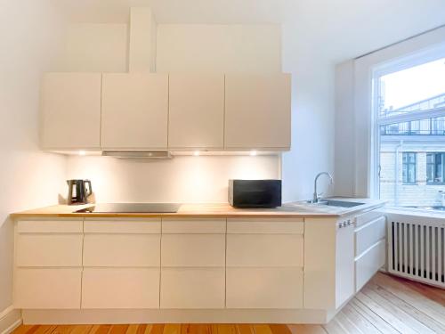 cocina con armarios blancos, fregadero y ventana en Large & Modern 4 Bedroom Flat, en Copenhague