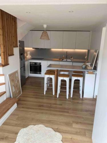 une cuisine avec des placards blancs, une table et des tabourets dans l'établissement Jolie Maison à 5mins des plages et du lac, à Soorts-Hossegor