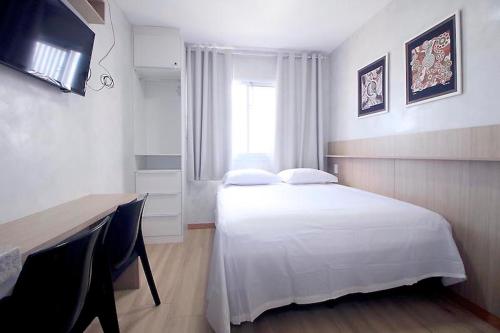 a bedroom with a white bed with a desk and a window at Refúgio acolhedor Praia e comércio à porta in Salvador