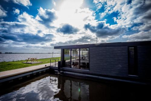 a house with a pond in front of a body of water at Vakantiewoonboot De Waterparel in Offingawier