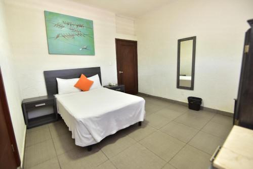 a bedroom with a white bed with an orange pillow at Bed Bed Hotel Perla in Torreón