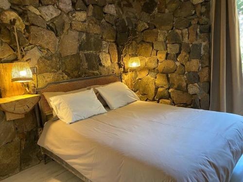 1 cama con 2 almohadas y pared de piedra en Iluminada casa de piedra entre bosque y río, en Lo Barnechea