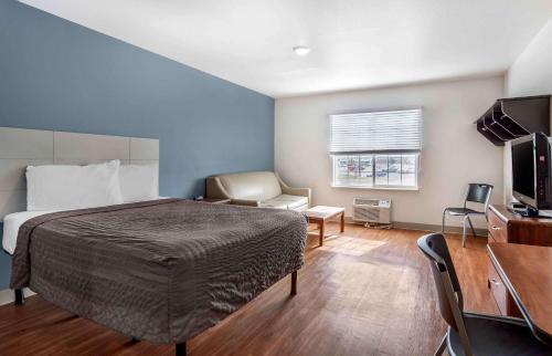Extended Stay America Select Suites - Wichita - South في ويتشيتا: غرفة نوم بسرير وكرسي وتلفزيون