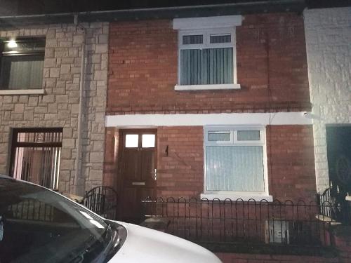 una casa de ladrillo con una puerta y un coche aparcado delante en Máire Toiréasa – cosy refurbished property in the Gaeltacht Quarter, en Belfast