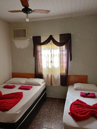 two beds in a room with a window with red sheets at Casa Vó Amélia in Aparecida