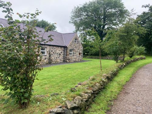 a stone house with a stone wall next to a yard at RB Contractor Stays - Dderwen in Pwllheli