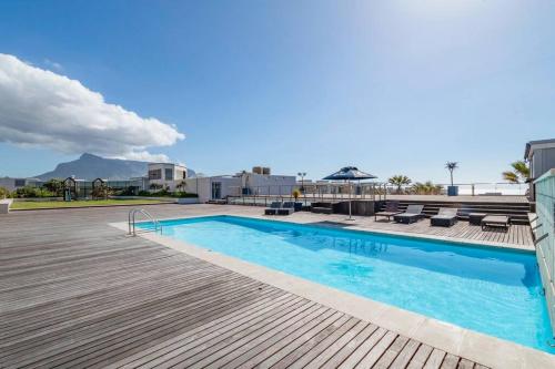 a swimming pool with a wooden deck next to a building at Oceanfront Residence in Lagoon Beach in Cape Town