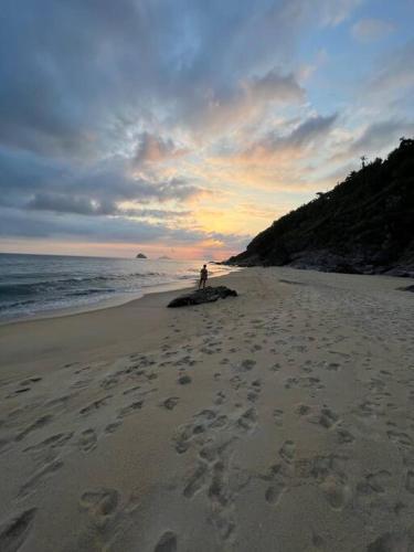 a person standing on a beach with footprints in the sand at Condomínio pé na areia, super novo e confortável. in São Sebastião